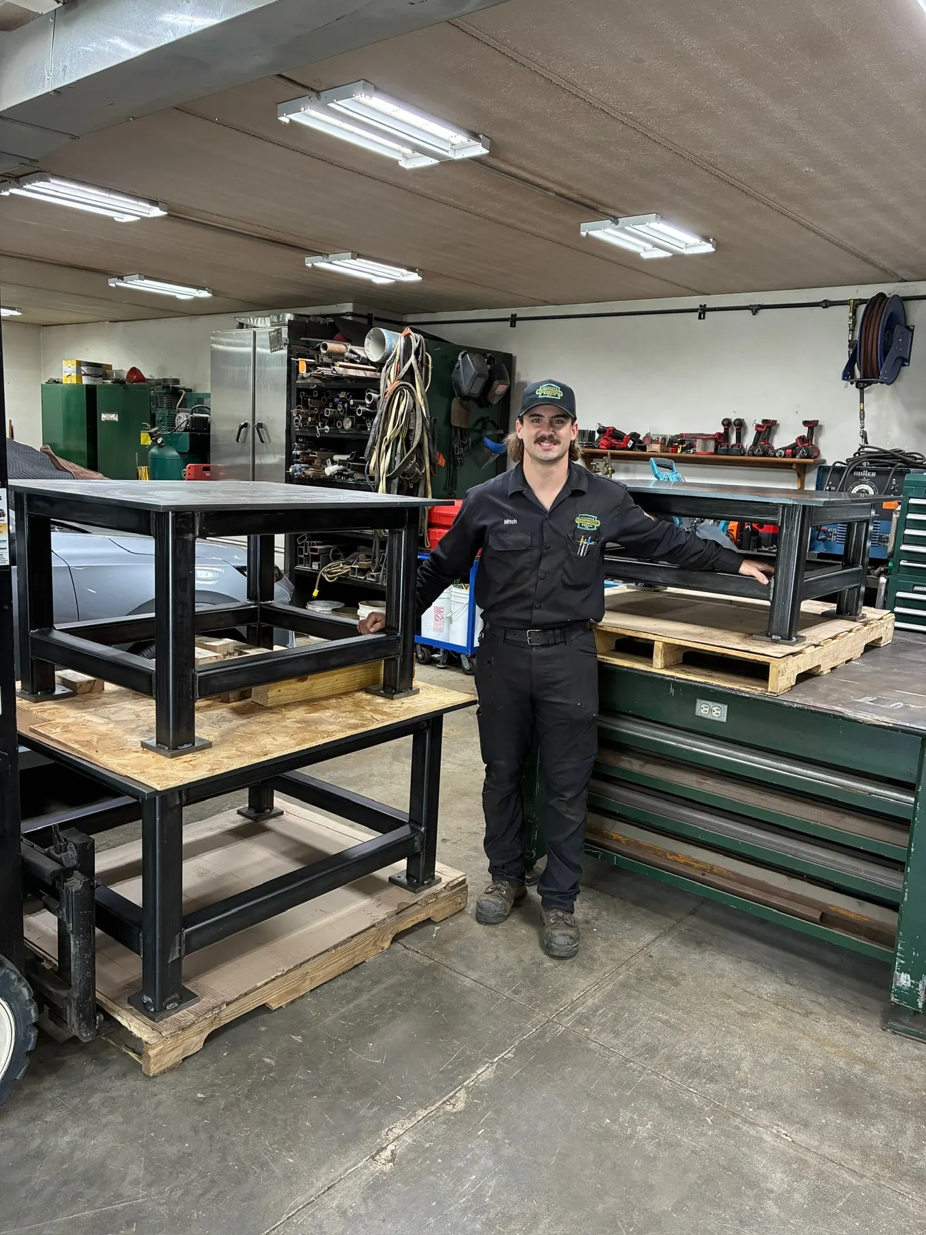 Schumacher Machine Repair team member standing beside custom-welded steel workbenches in the fabrication shop.